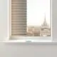 Panel de persianas metálicas en una ventana blanca, con un skyline de Barcelona al fondo. Donde puedo contratar la instalacion de persianas metalicas de manera rapida en Barcelona.
